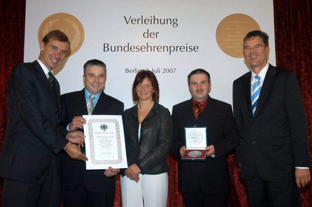 DLG-Pr&auml;sident Carl-Albrecht Bartmer (links) &uuml;berreicht gemeinsam mit dem Parlamentarischen Staatssekret&auml;r Dr. Gerd M&uuml;ller (rechts) Urkunde und Medaille an das Inhaberehepaar Erich und Karola Kanefzky sowie Produktionsleiter Markus Dei&szlig;er (2.v.r.).